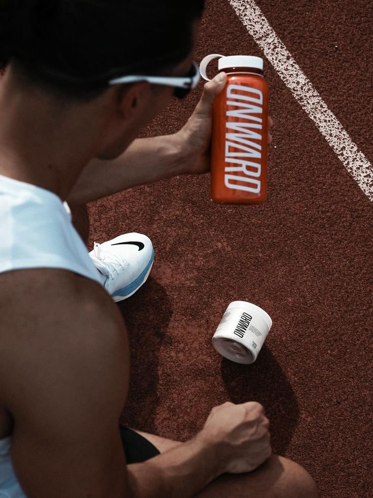 Athlete crouched on a running track holding an orange drink bottle