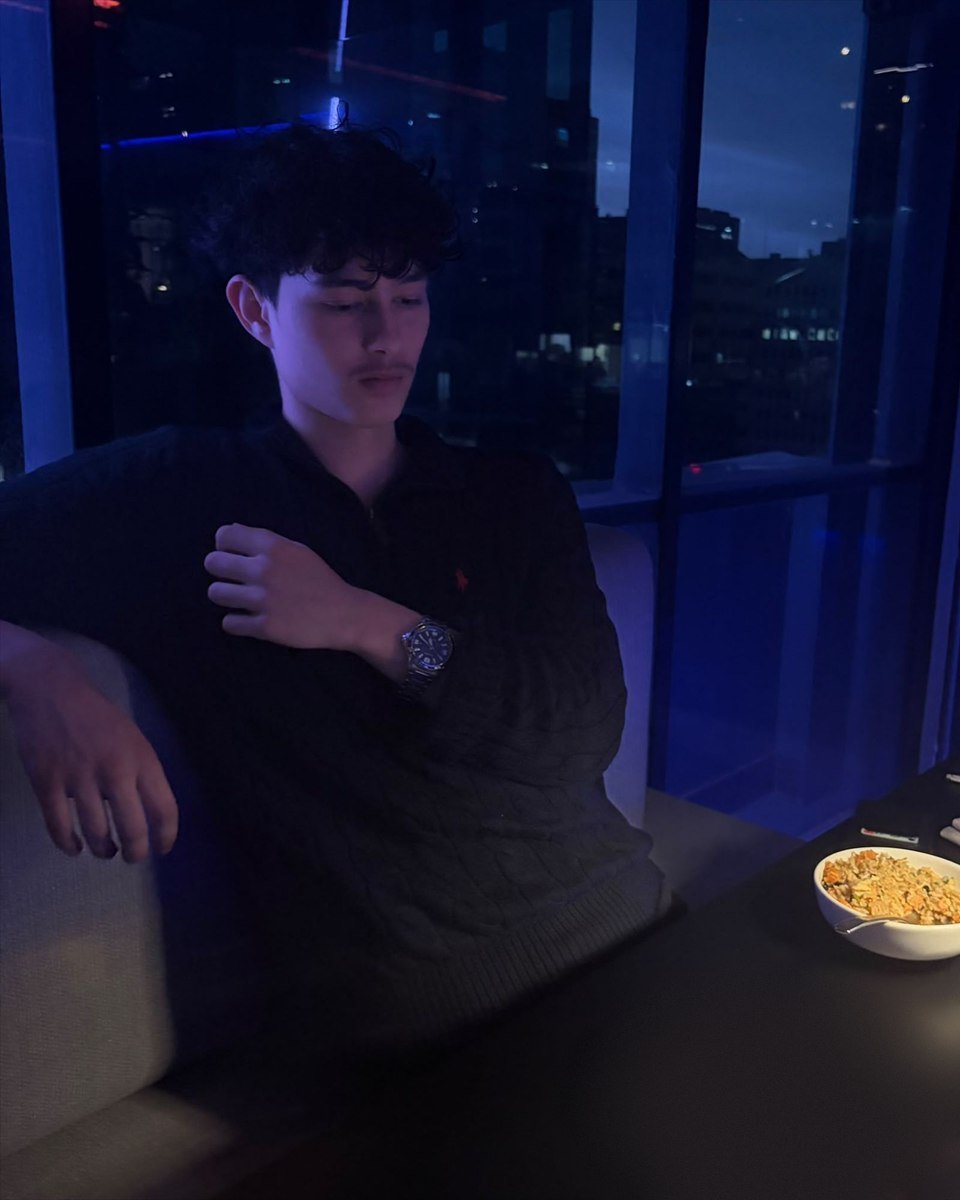Cengizhan Subasi sitting at a table by a window with a night city view behind him